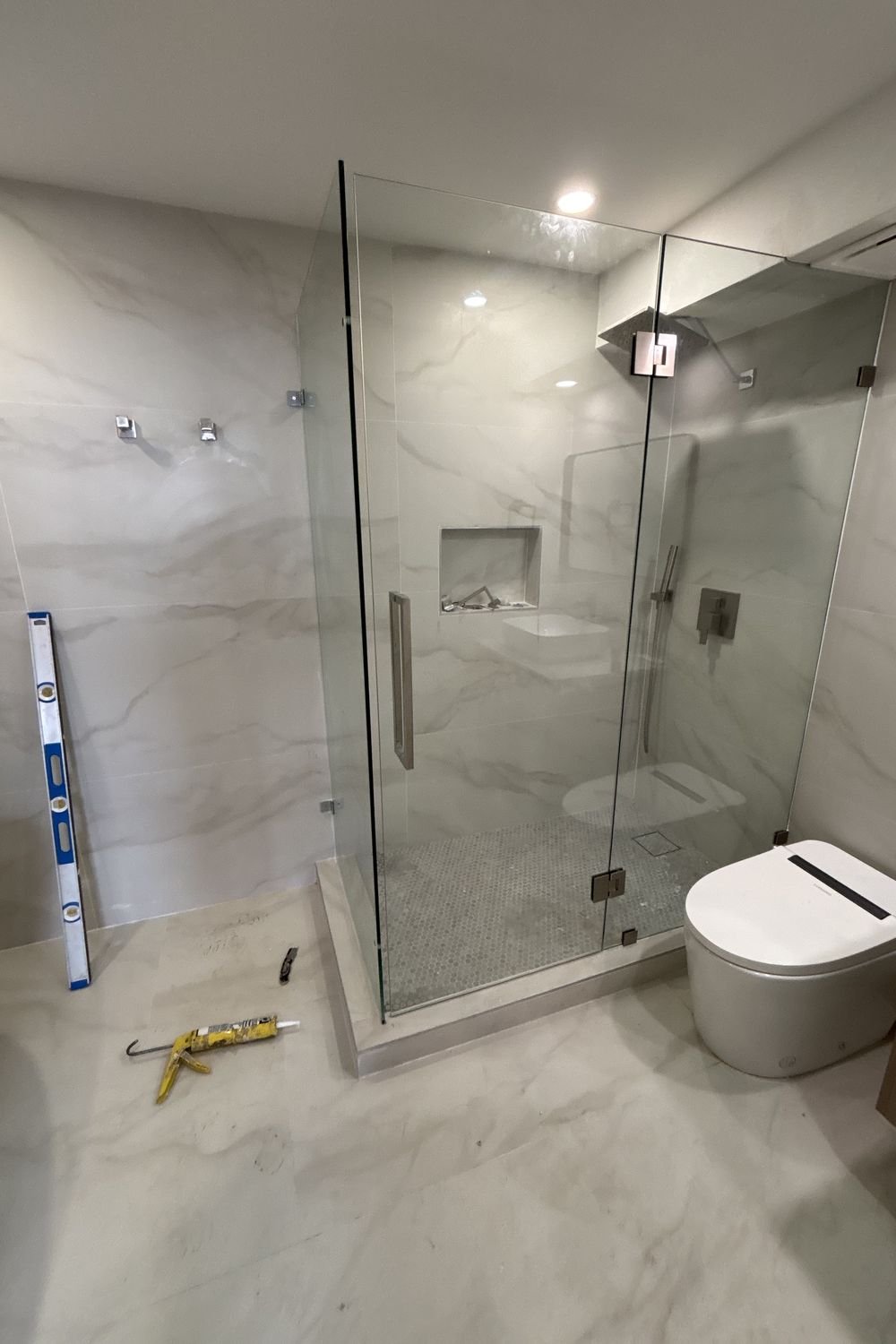 Finished bathroom with a frameless glass corner shower, marble-look porcelain walls and floor, a built-in bench and a floating wood vanity.