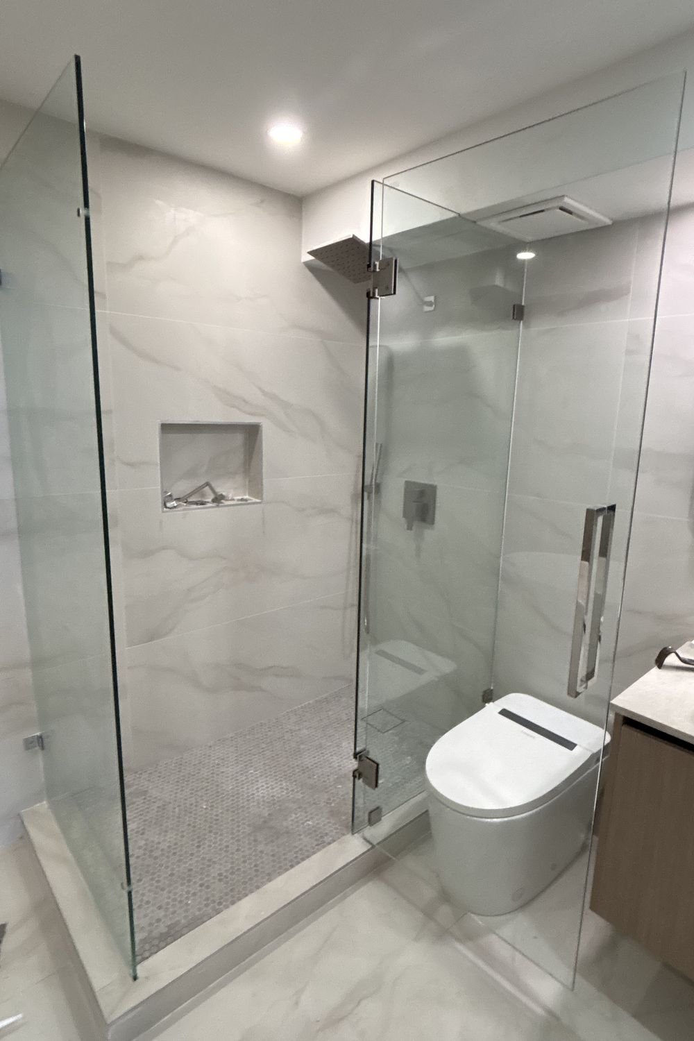 Close view of the same shower showing the recessed niche, the ceiling rain head, the wall mixer and the mosaic shower floor.