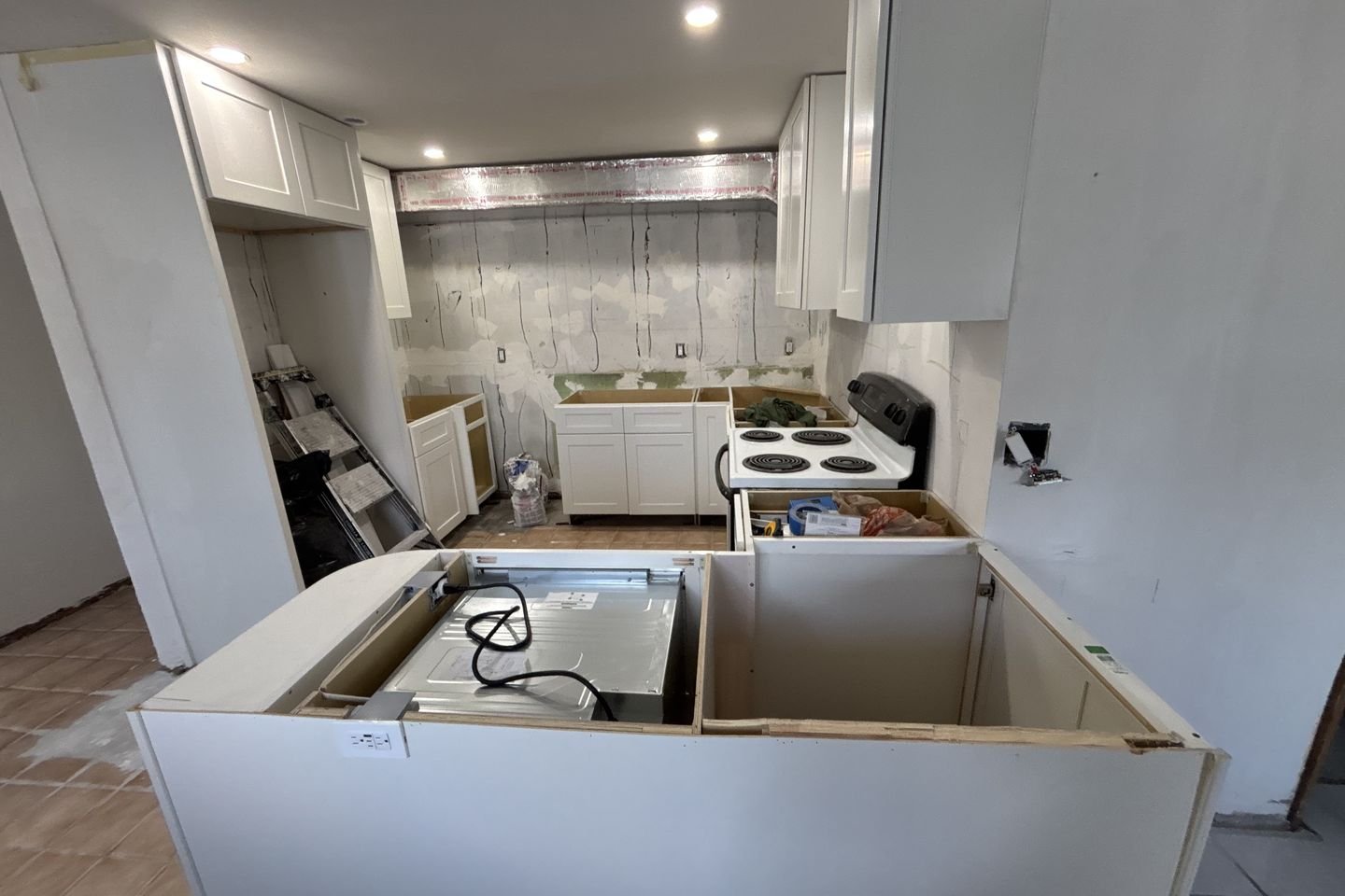 The same kitchen mid-job, with new white shaker cabinets hung and the peninsula base framed but not yet finished.