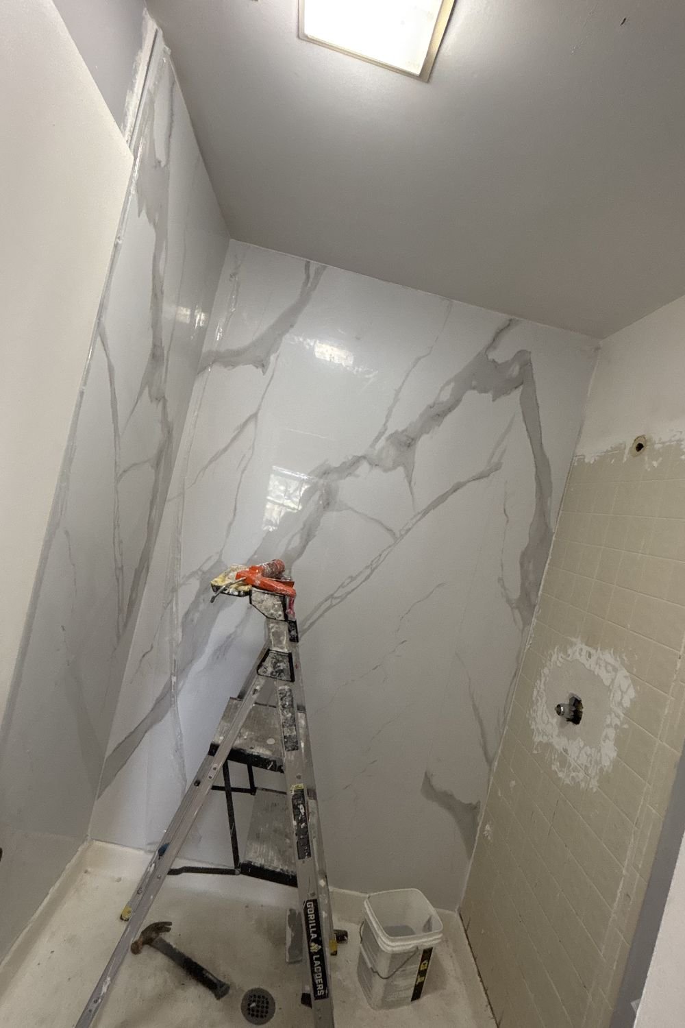 The same shower part-way through re-tiling in large-format marble-look porcelain, with the original small tile still on the right wall.